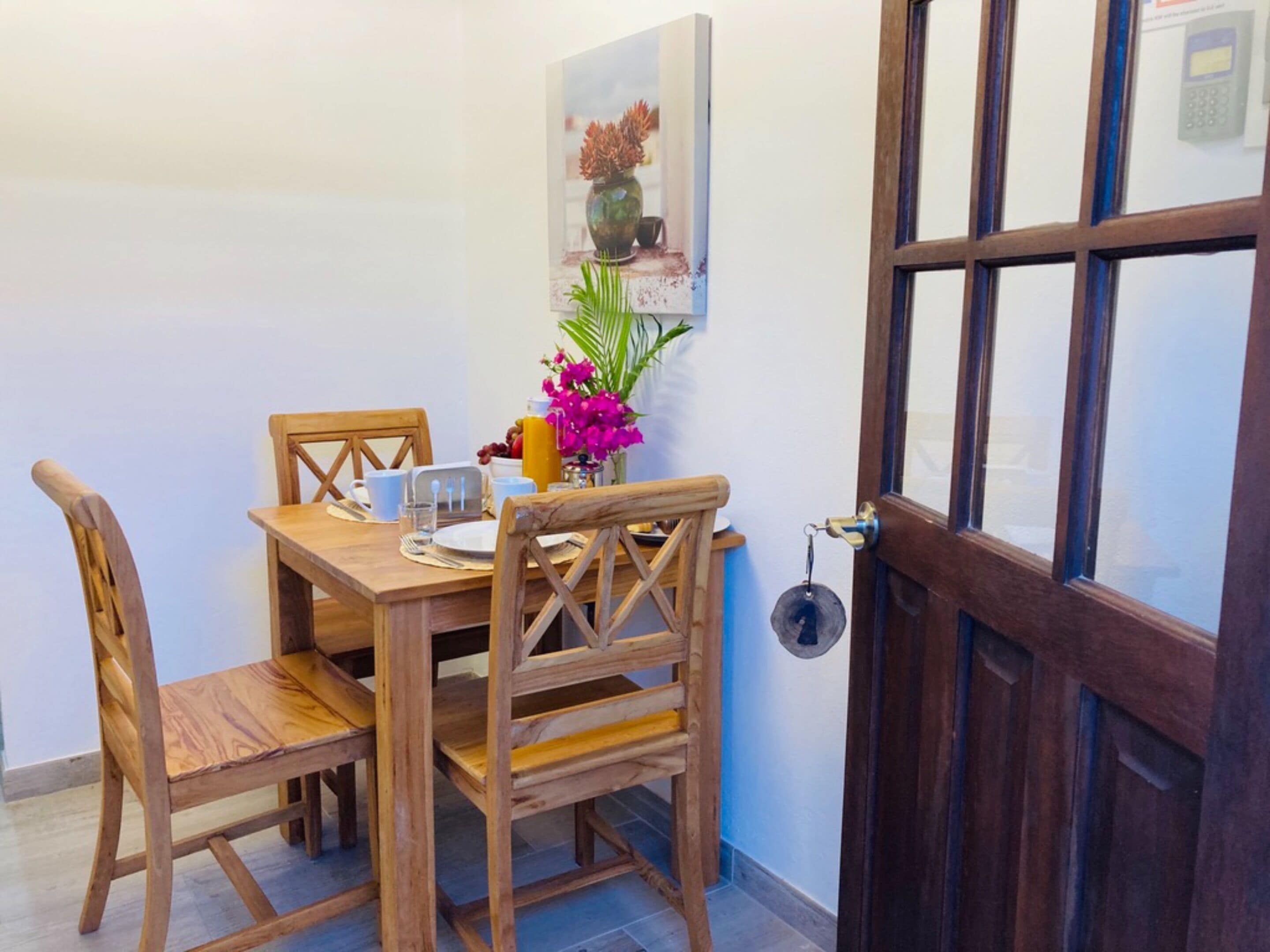 Una mesa de comedor de madera con sillas, un jarrón con flores y un cuadro en la pared.