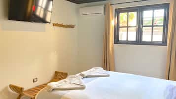 Habitación de hotel con cama, televisor montado en la pared, ventana con cortinas y una silla de madera.