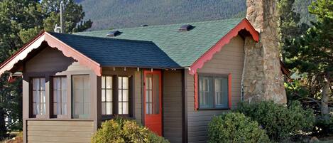 A small cabin with a stone chimney, a red door, and a green roof.