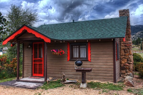 A rustic cabin with a red door, stone chimney, and a small porch.
