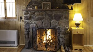 A stone fireplace with a decorative metal door, a wooden mantel shelf with a picture frame, and a table lamp to the right. - Tiny Town Cabins (Estes Park)