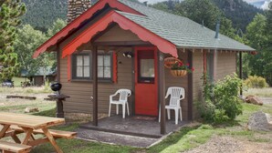 A small cabin with a red door, two white plastic chairs outside, and a picnic table. - Tiny Town Cabins (Estes Park)