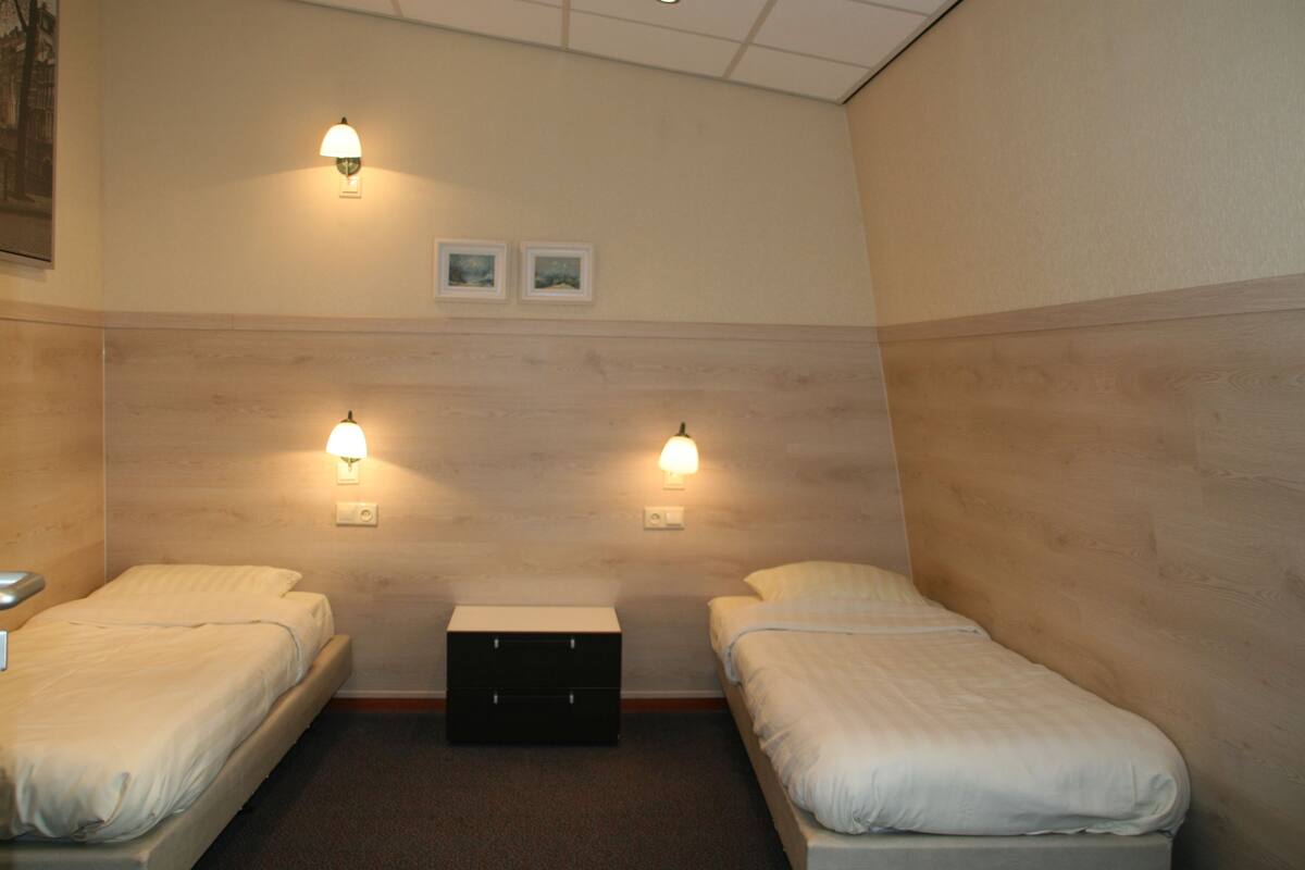 A hotel room with two single beds, a small dresser, and two wall-mounted lamps.