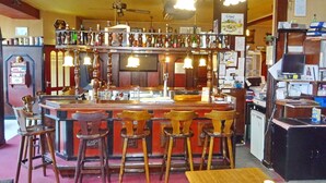 A bar area with wooden stools, a counter, and various bottles and glasses. - Hotel Het Galjoen (Dronten)