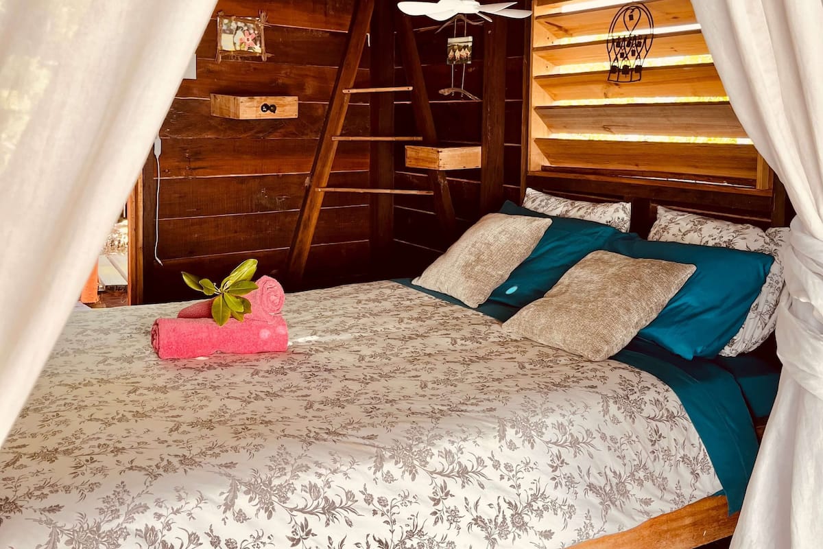 Une chambre confortable, aménagée dans un chalet en bois, avec un lit, des oreillers et un ventilateur de plafond.