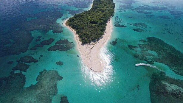 Luchtbeeld van een tropisch eiland met een zandstrand en helder turquoise water.