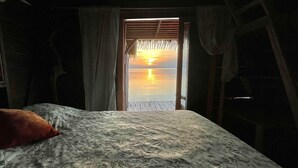 Een kamer met een bed en uitzicht op een zonsondergang boven water.