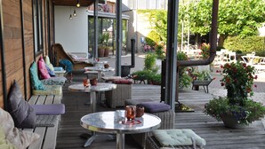 An outdoor patio with wicker furniture, round tables, and potted plants. - Droste's herberg (Tubbergen)