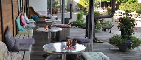 An outdoor patio with wicker furniture, round tables, and potted plants.