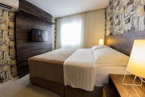 A hotel room with a large bed, a flat-screen TV mounted on the wall, and a patterned wallpaper on the left side.