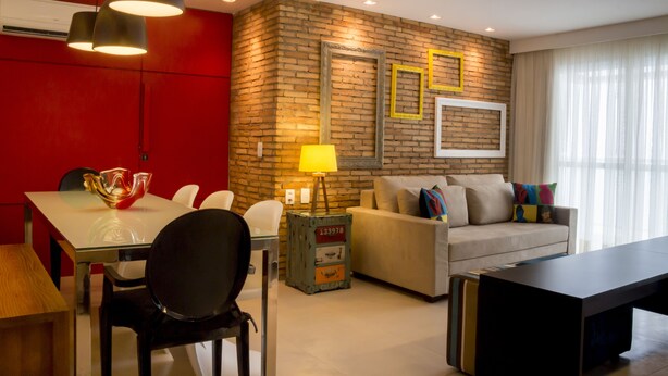 Uma sala de estar moderna com parede de tijolos, um sofá, uma mesa de centro e um espaço de jantar com cadeiras e uma mesa de vidro.