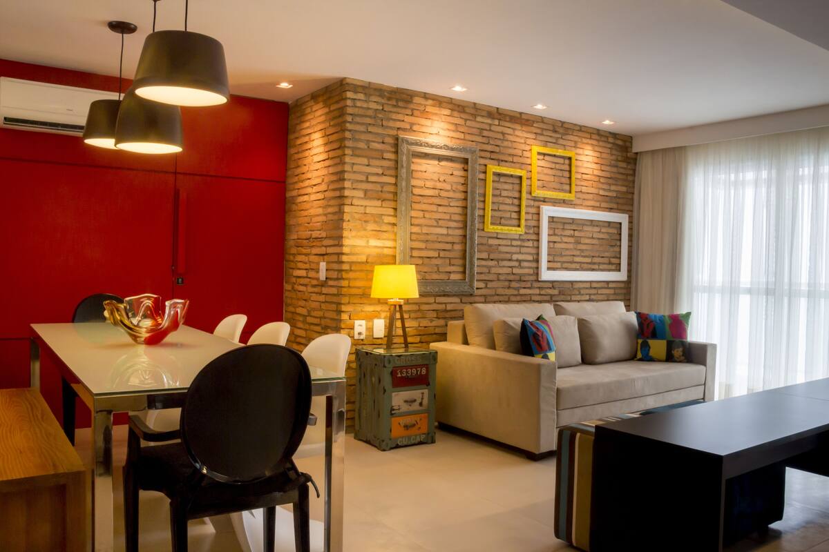 Una sala moderna con una pared de ladrillo decorativa, un sofá, una mesa de centro y un comedor con sillas y una mesa de vidrio.