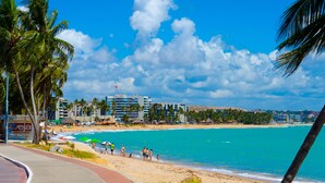 Uma praia com palmeiras, céu claro e edifícios ao fundo.