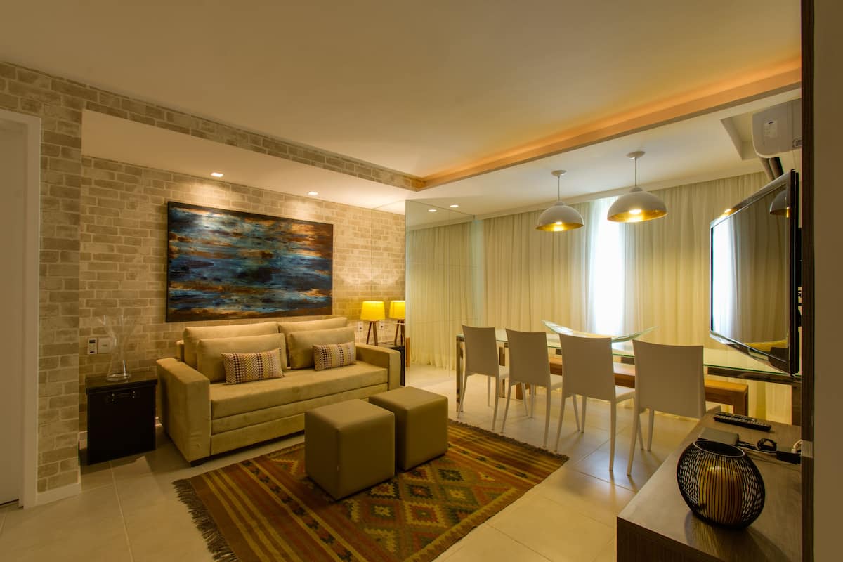 Una sala de estar moderna con un sofá, otomanas, una mesa de centro, un comedor con sillas, un televisor y un cuadro en la pared.