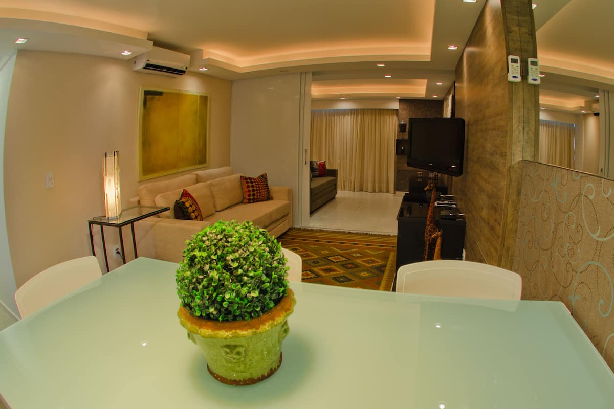 Una habitación de hotel moderna con una mesa de comedor de vidrio, un sofá, un televisor y una pequeña planta en maceta.