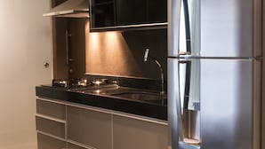 Cozinha moderna com geladeira de aço inoxidável, fogão a gás e forno embutido. Há plantas em vasos sobre o balcão e uma prateleira acima do fogão.