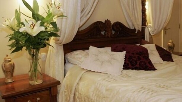 A bedroom with a four-poster bed, white bedding, a vase of flowers on a nightstand, and a lamp. - The Bull Inn (Shrewsbury)