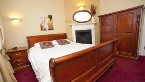 A bedroom with a wooden bed, a nightstand, a dresser, a fireplace, and a wall-mounted mirror. - The Bull Inn (Shrewsbury)