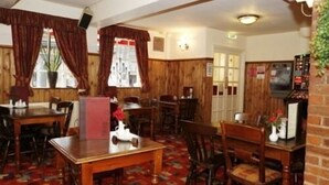 A restaurant with wooden walls and a patterned carpet. Tables and chairs are arranged for dining. - The Bull Inn (Shrewsbury)