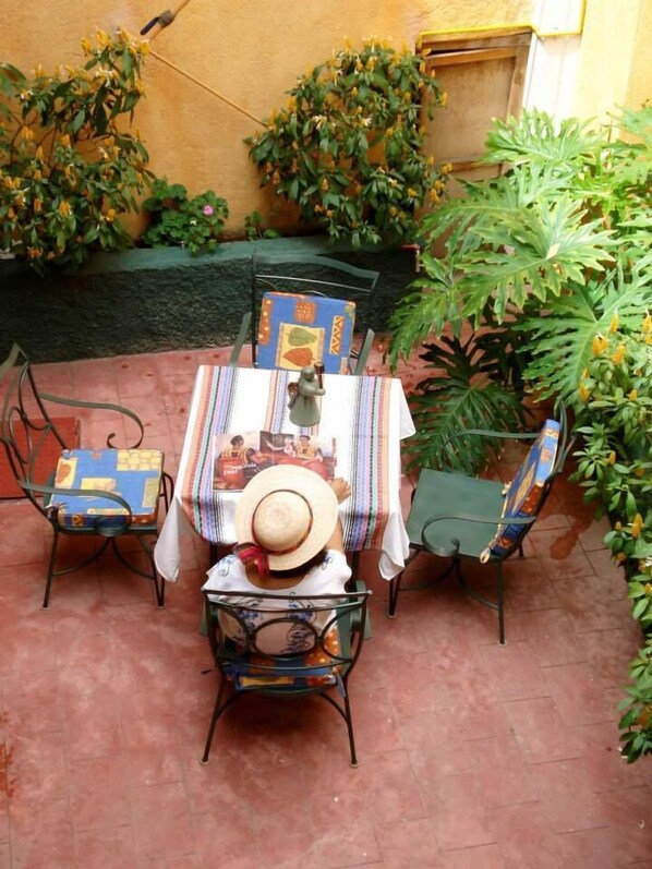 An outdoor patio with a table set for two, surrounded by chairs with patterned cushions.