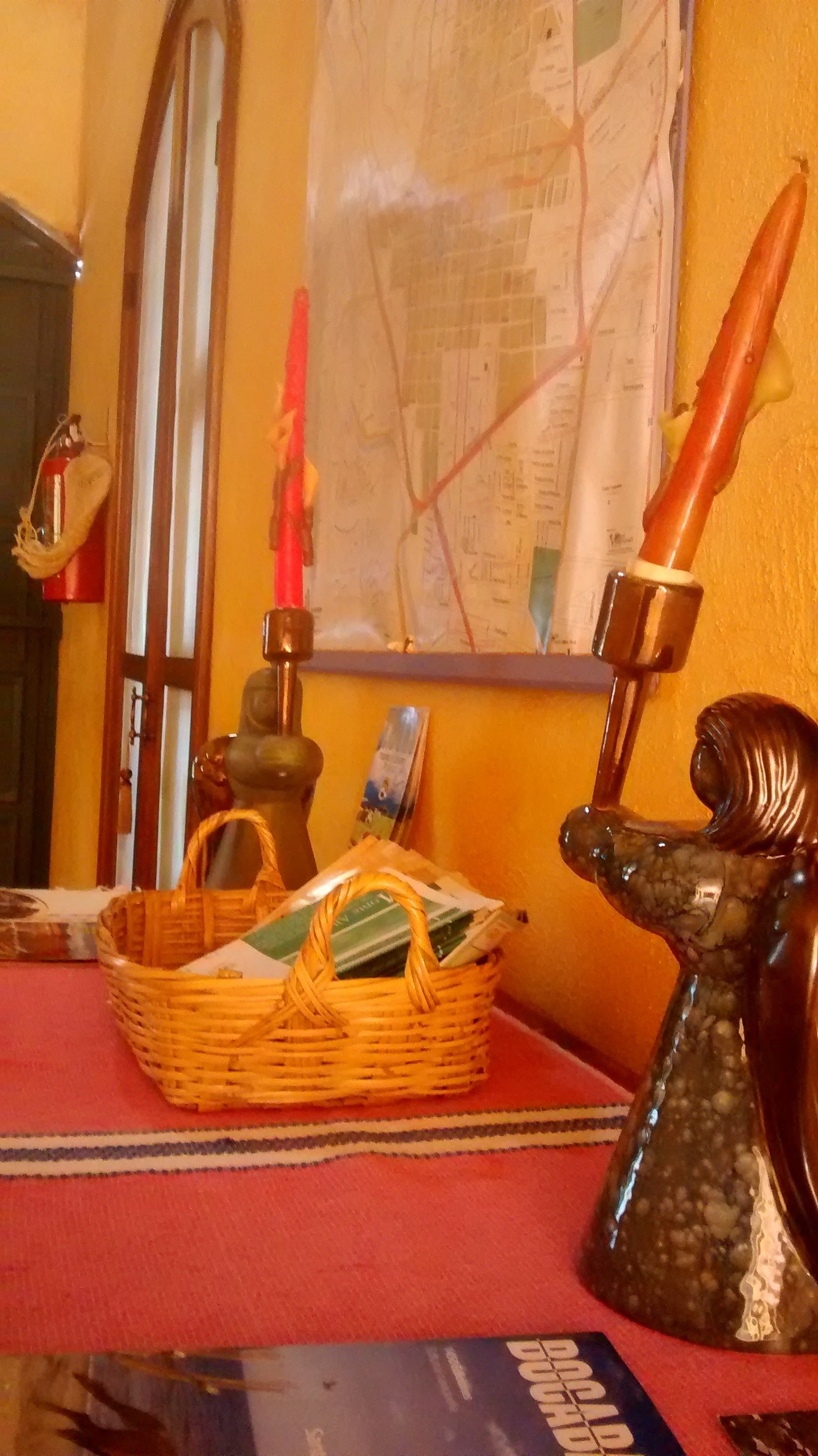 A room with a map on the wall, a wooden table with a basket, a candle holder, and a decorative metal object.