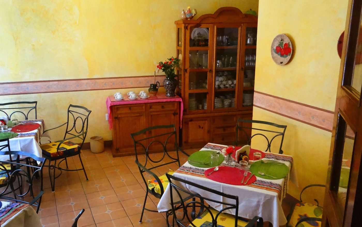 A dining area with a table set for two, a cabinet with glass doors, and a wall-mounted plate with fruit design.