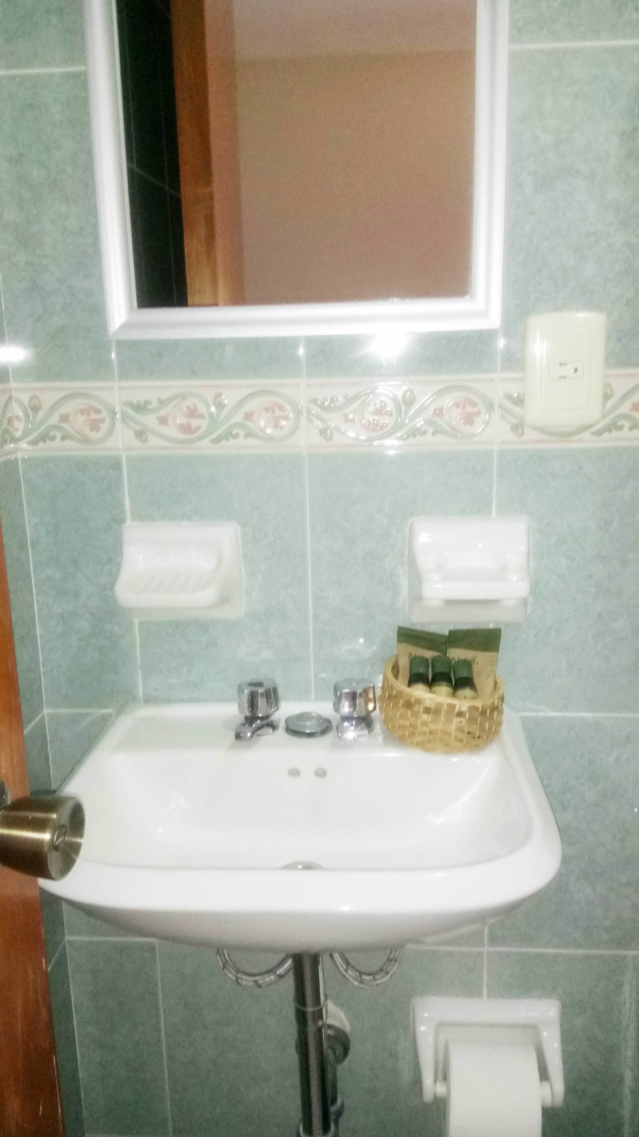 A bathroom with a white sink, a mirror above it, and a toilet paper holder to the right.