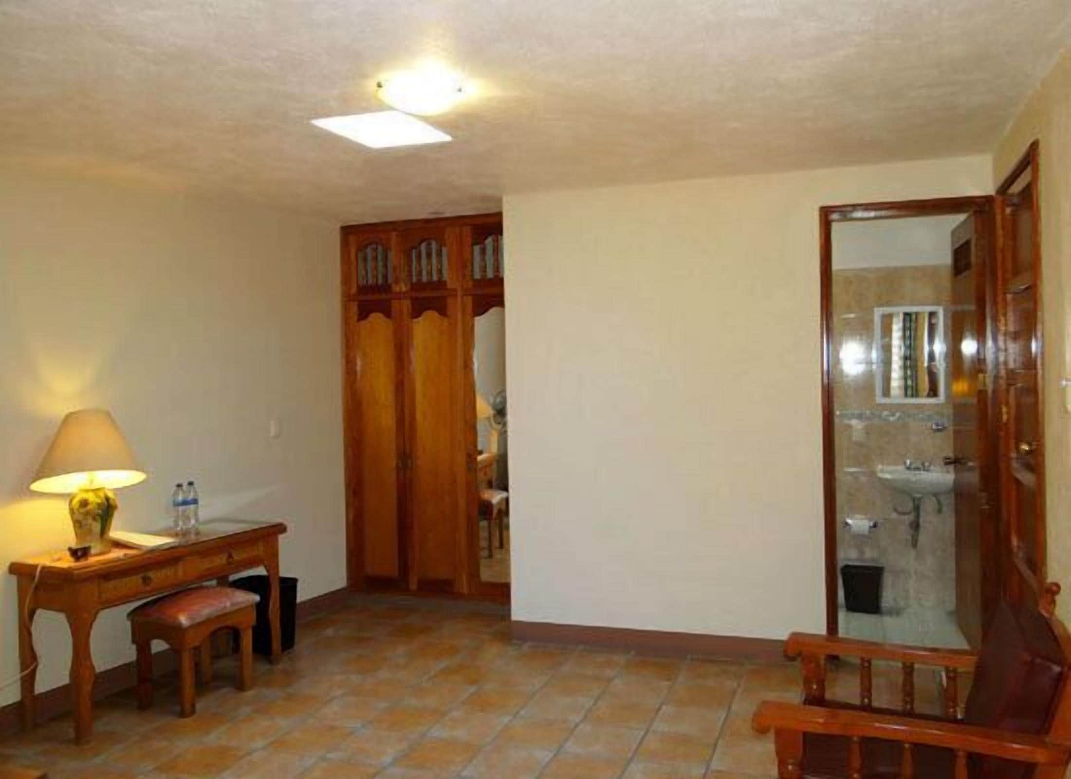 A room with a wooden desk, a bench, a mirror, and a tiled floor.