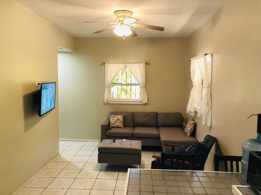 A living room with a sofa, ottoman, and a TV mounted on the wall.