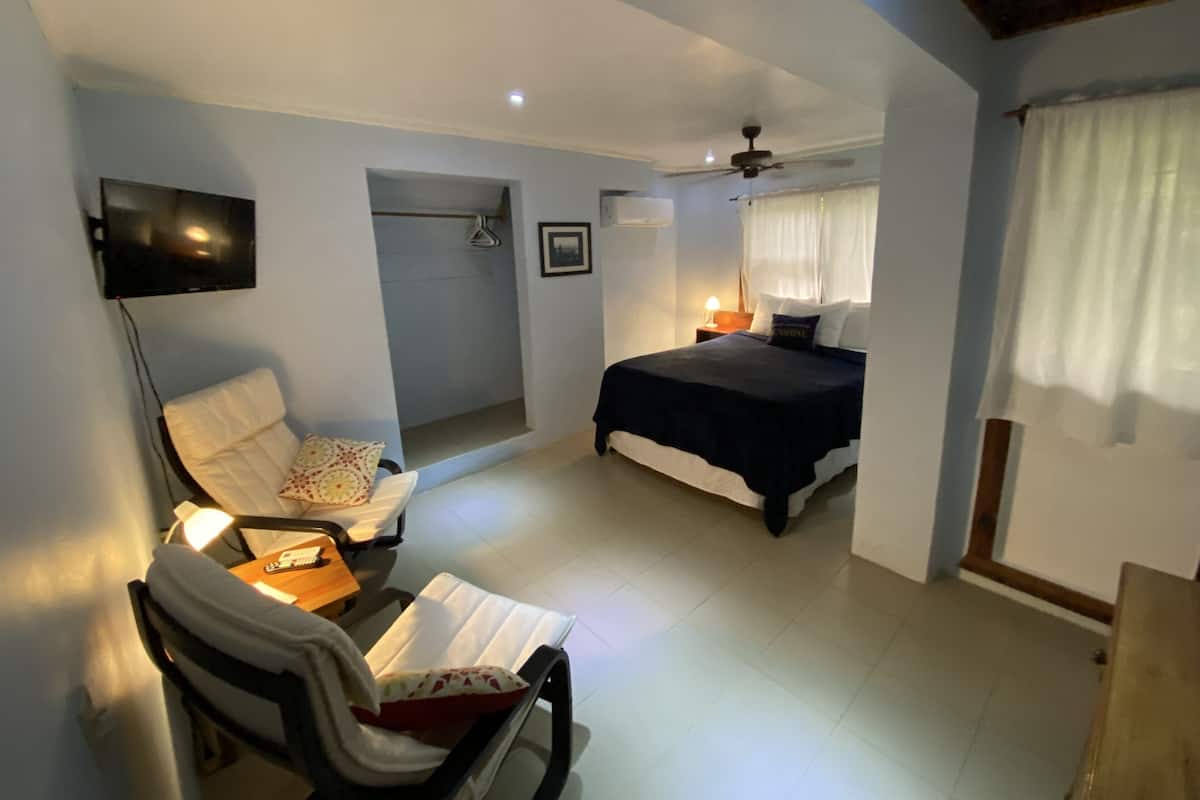 Ein Schlafzimmer mit Bett, Stuhl, Schreibtisch, Fernseher und Deckenventilator.