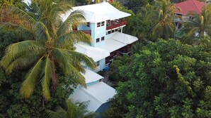 A multi-story building with a white roof and blue walls, surrounded by dense tropical vegetation. - Mariposa Lodge (Roatan)