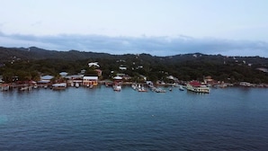 A coastal town with a marina, buildings, and hills in the background. - Mariposa Lodge (Roatan)