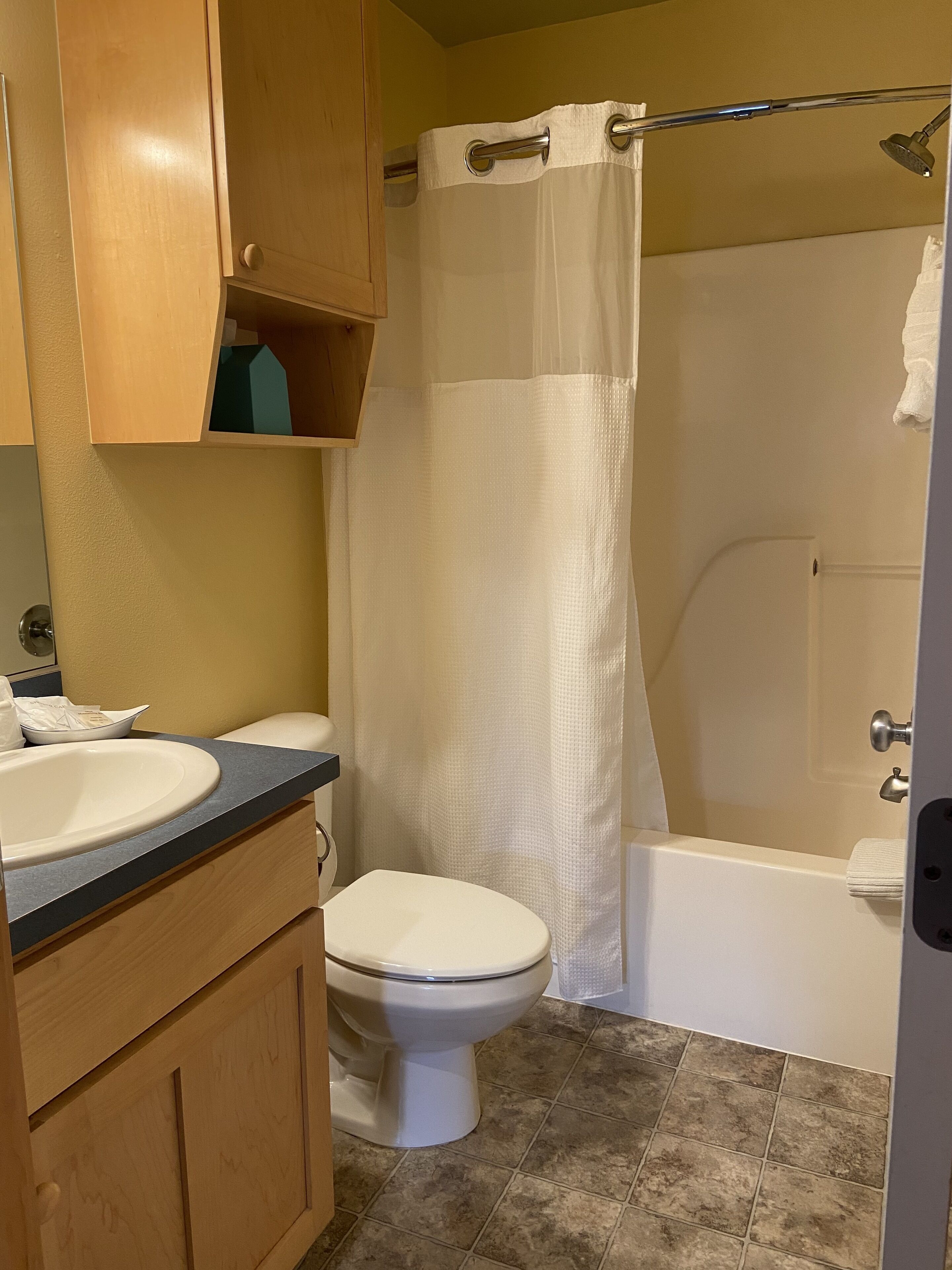 A bathroom with a toilet, sink, shower, and wooden cabinets.