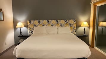 Hotellihuone, jossa on suuri sänky, kaksi yöpöytälamppua, puhelin ja lasiovi.