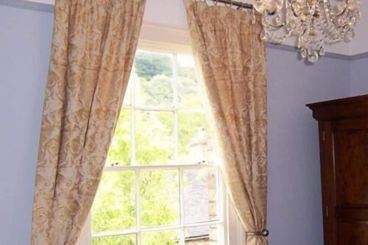 Una habitación con un ventanal grande, cortinas y una araña.
