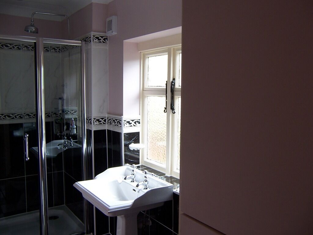 A bathroom with a glass-enclosed shower, a white sink, and a window with a view.