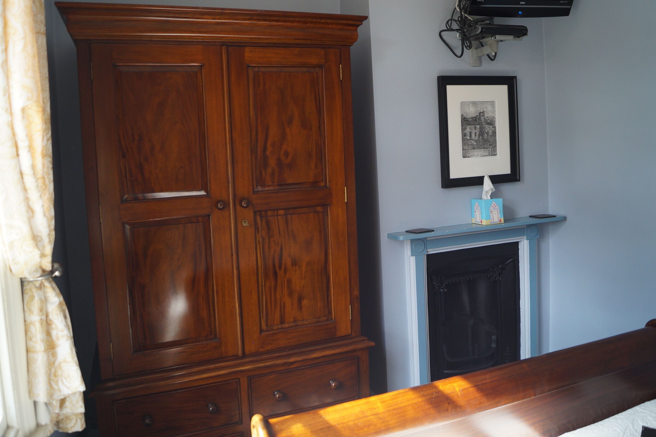 Une pièce avec une grande armoire en bois, un tableau encadré au mur et une cheminée avec un manteau bleu.