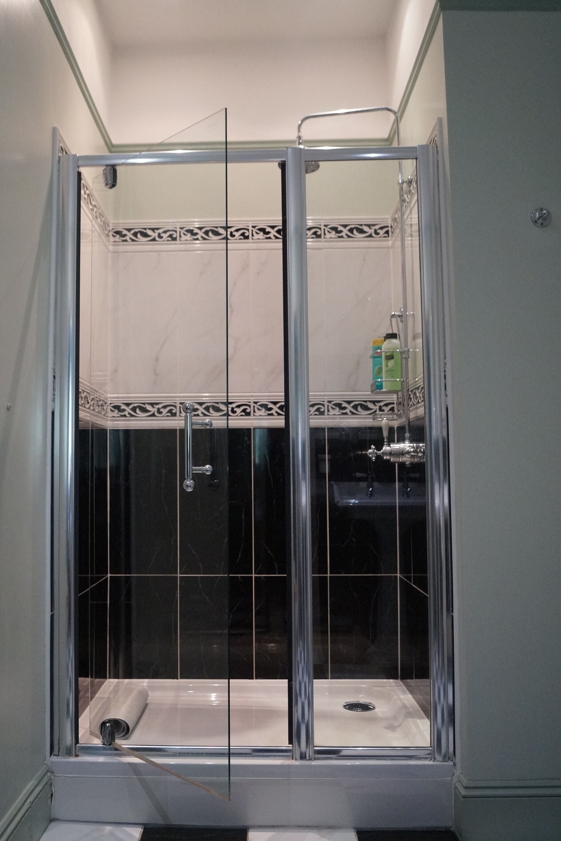 A glass-enclosed shower with a white sink and a decorative tile border.