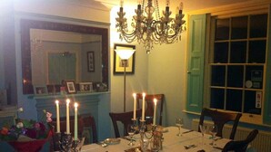 Ein Esszimmer mit gedecktem Tisch für vier Personen, Kerzen, einer Kristallleuchtre und einem Spiegel.