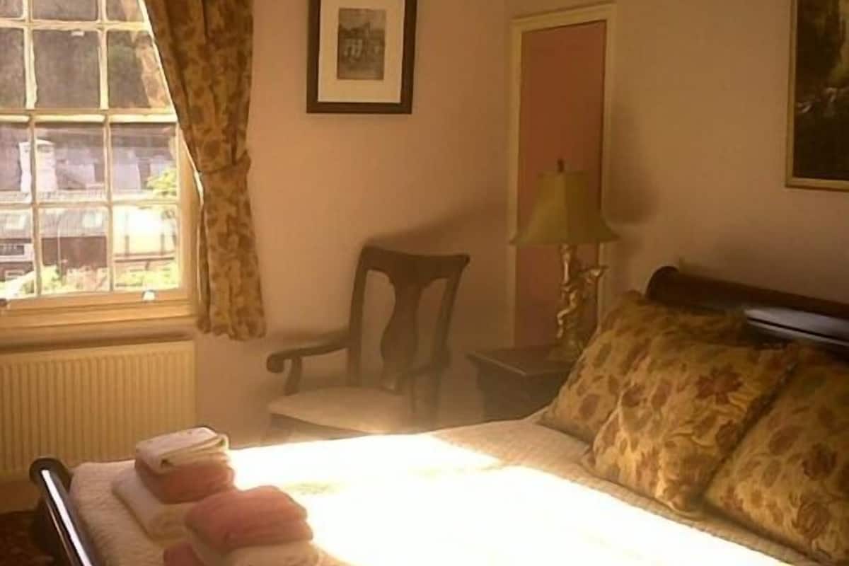 Un dormitorio con cama, una silla, una lámpara y una ventana con cortinas.
