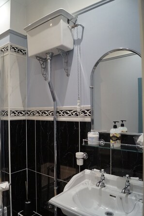 A bathroom with a white sink, black marble tiles, a glass shelf with toiletries, and a white toilet.