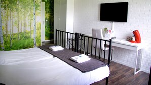 Une chambre d’hôtel équipée d’un lit, d’un bureau, d’une chaise, d’une télévision et d’un mur décoré d’une fresque représentant un paysage naturel.