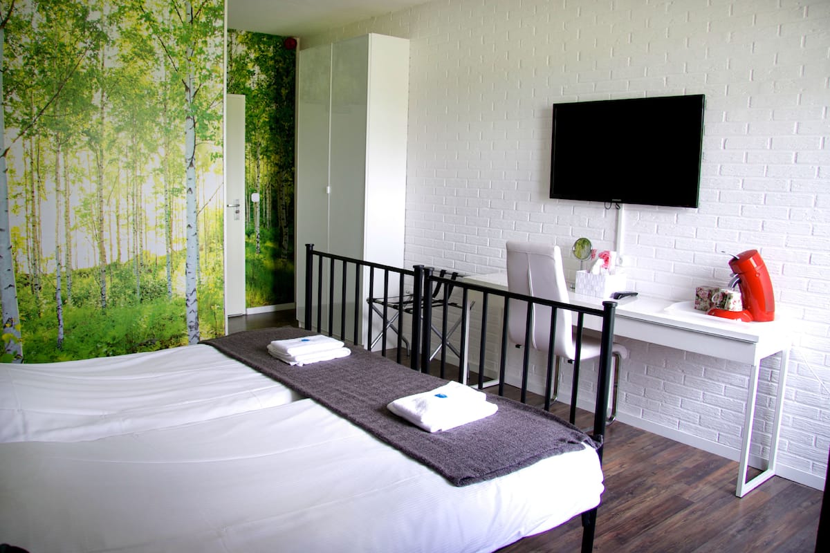 A hotel room with a bed, a desk, a chair, a television, and a wall with a nature mural.