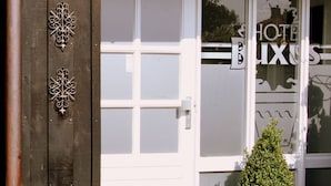 L’entrée d’un hôtel avec une porte blanche, des éléments décoratifs en métal, un mur en pierre et un pot de fleurs.