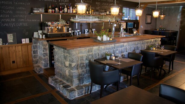 Un espace bar doté d’un comptoir en pierre, de plusieurs luminaires suspendus et d’un menu affiché au mur, indiquant une variété de boissons et de desserts.