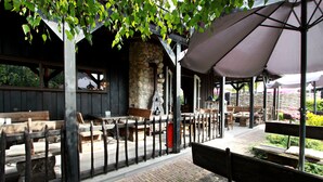 Un espace extérieur aménagé en terrasse, avec des bancs et des tables en bois, des murs en pierre et un coin salon couvert équipé de parasols.