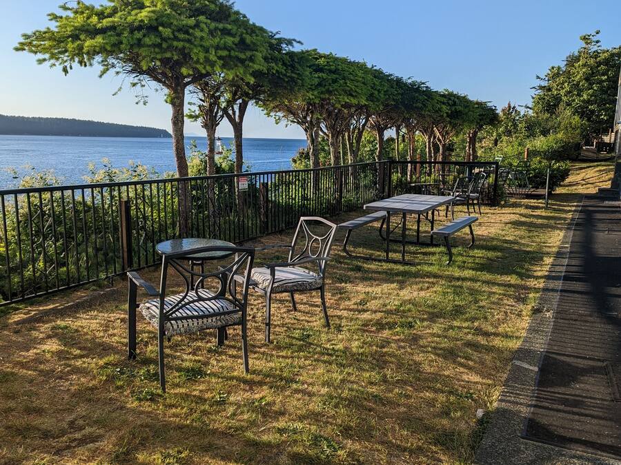 An outdoor seating area with tables and chairs, a metal fence, and a view of the sea.