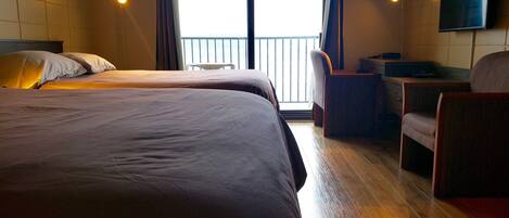 Habitación de hotel con dos camas, un escritorio, una silla y un televisor en la pared.