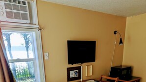 A hotel room with a wooden dining table, two chairs, a TV mounted on the wall, a microwave on a small table, and a bed with patterned bedding. - Above Tide Motel (Campbell River)