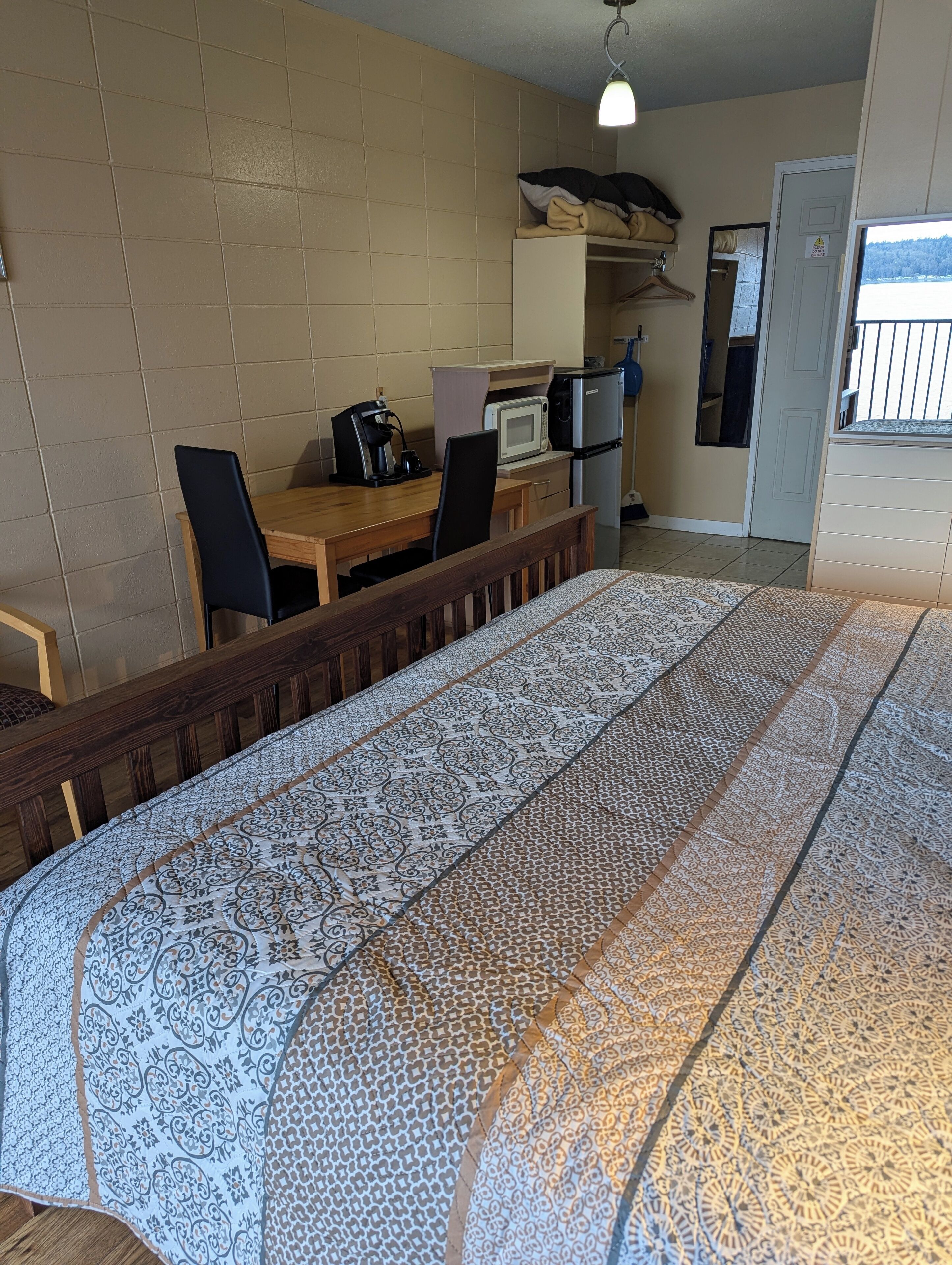 A room with a bed, a desk, a chair, a microwave, a refrigerator, and a door leading to a balcony.